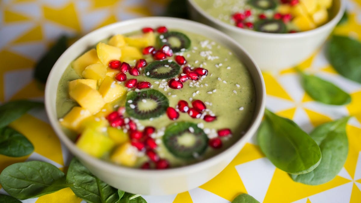 Delicious green smoothie bowl topped with kiwi, pomegranate, and mango on a vibrant background.